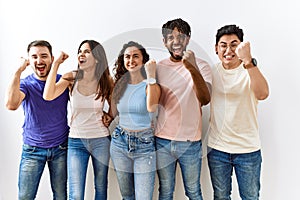 Group of young people standing together over isolated background angry and mad raising fist frustrated and furious while shouting