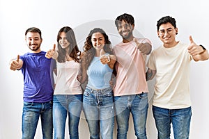 Group of young people standing together over isolated background approving doing positive gesture with hand, thumbs up smiling and