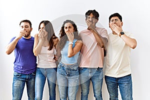 Group of young people standing together over isolated background bored yawning tired covering mouth with hand