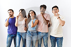 Group of young people standing together over isolated background with hand on chin thinking about question, pensive expression