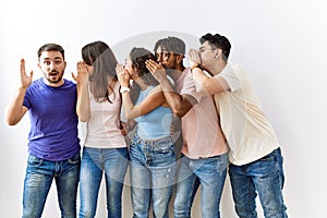 Group of young people standing together over isolated background hand on mouth telling secret rumor, whispering malicious talk