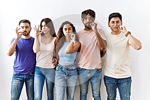 Group of young people standing together over isolated background mouth and lips shut as zip with fingers