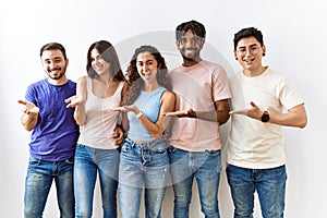 Group of young people standing together over isolated background pointing aside with hands open palms showing copy space,