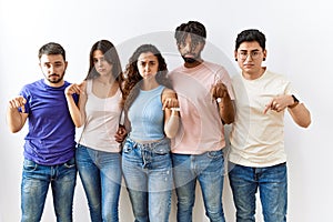 Group of young people standing together over isolated background pointing down looking sad and upset, indicating direction with