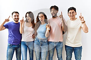 Group of young people standing together over isolated background pointing finger up with successful idea