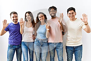 Group of young people standing together over isolated background waiving saying hello happy and smiling, friendly welcome gesture