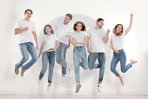 Group of young people in stylish jeans jumping near wall