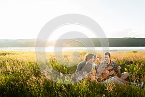 Group of young people in sundown playing guitar music