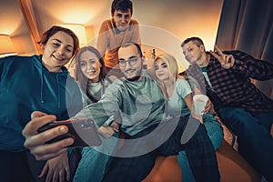 Group of young people taking selfie on smartphone at home party and have fun. Friends enjoy their company, smiling
