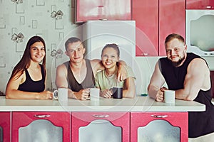 Group of young people in their 20s met in kitchen for tea, two married couples in front of kitchen island.