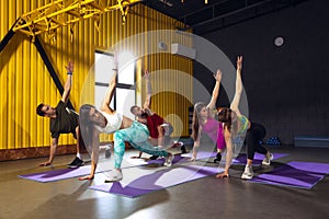 Group of young people training at gym, doing stretching and yoga exercises indoors