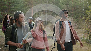 Group of young people travelers hiking in forest holding map talking and gesturing
