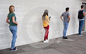 Group of young people waiting for going inside a shop market while keeping social distance in a line during coronavirus time -