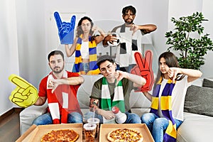 Group of young people wearing team scarf cheering football game with angry face, negative sign showing dislike with thumbs down,