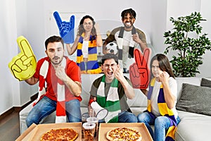 Group of young people wearing team scarf cheering football game annoyed and frustrated shouting with anger, yelling crazy with