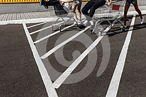 A group of young people in white t-shirts, fun ride on carts near the store, supermarket, friends have fun in Sunny weather