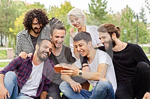 A group of young people are working in the park with mobile phones.They all laugh looking at the phone