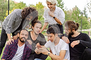 A group of young people are working in the park with mobile phones.They watch the phone carefully photo