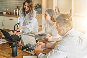 Group of young people working together.Man is using laptop,girls looking on screen of laptop,discussing business plan.