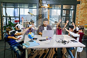 Group of young pupils of elementary school using virtual reality glasses during computer coding class.