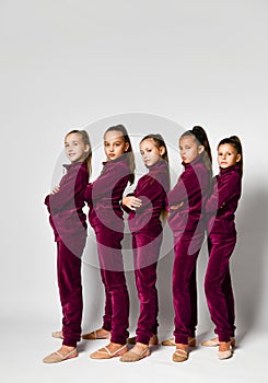 Group of young smiling girls gymnasts in dark red velvet sport costumes standing and posing over white background
