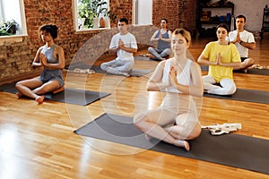 Group of young sporty attractive people practicing yoga lesson with instructor. Multi ethnic women and men sit together in pose