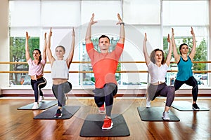 Group of young sporty attractive people practicing yoga lesson with instructor, standing together in exercise, working