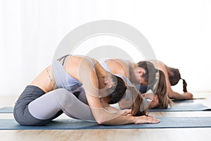 Group of young sporty attractive women in yoga studio, practicing yoga lesson with instructor, sitting on floor in