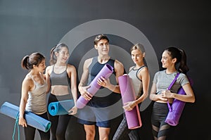 Group of young sporty people with fitness yoga exercise mats standing beside black wall.Students taking a rest from fitness