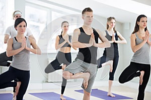 Group of young sporty people in Vrksasana pose