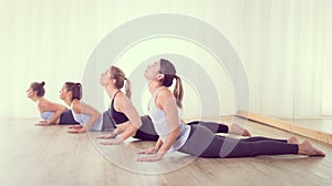 Group of young sporty sexy women in yoga studio, practicing yoga lesson with instructor, forming a line in asana pose