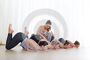 Group of young sporty sexy women in yoga studio, practicing yoga lesson with instructor, forming a line in front bent