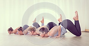 Group of young sporty sexy women in yoga studio, practicing yoga lesson with instructor, forming a line in Shishosana