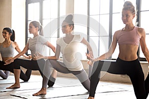 Group of young sporty women practicing yoga, doing anjaneyasana