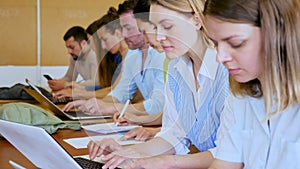 Group of young students searches for information on a laptop and writes it down in a copybooks, studying in a university