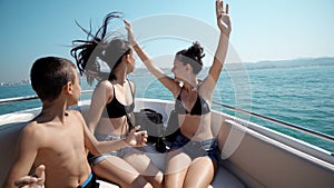 Group of young teen children partying and dancing on a sailing boat with hands up