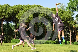 Group of young teenagers people in team wear playing a frisbee game in park oudoors. jumping man catch a frisbee to a teammate in