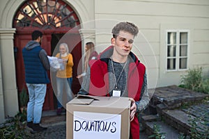 Group of young volunteers giving donation box to senior woman standing in door, social care concept