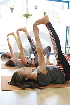 Group of young women exercising in yoga class, lying down in Supta Padangushthasana, a variation of reclined hand to big toe pose