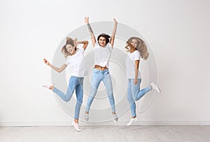 Group of young women in jeans jumping near wall