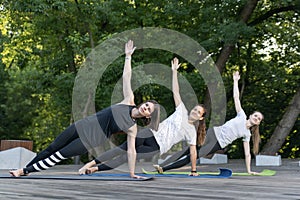 Group of young women practice yoga early in the morning outdoors. Side Plank. Vasishthasana