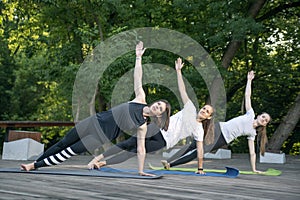 Group of young women practice yoga early in the morning outdoors. Side Plank. Vasishthasana