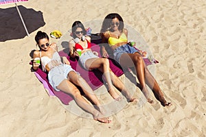 Group of young women resting on the beach, sunbathing on bright summer day