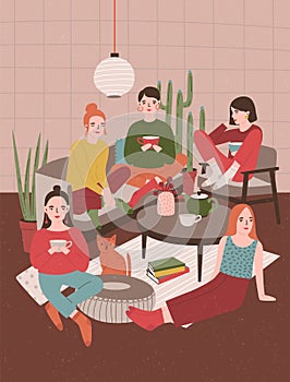 Group of young women sitting in room furnished in Scandinavian style, drinking tea and talking to each other. Girls