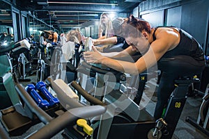 Group of young women in sportswear stretching their legs on exercise bikes before cycling class in gym