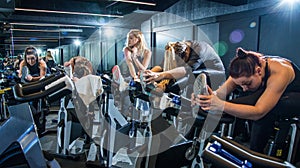 Group of young women in sportswear stretching their legs on exercise bikes before cycling class in health club