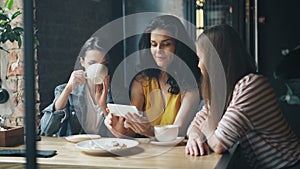 Group of young women watching smartphone screen laughing drinking coffee in cafe