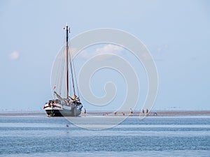 Group of youngsters on sand flat and flat-bottom sailboat at low