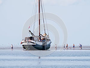 Group of youngsters on sand flat and flat-bottom sailboat at low