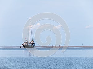 Group of youngsters on sand flat and flat-bottom sailboat at low